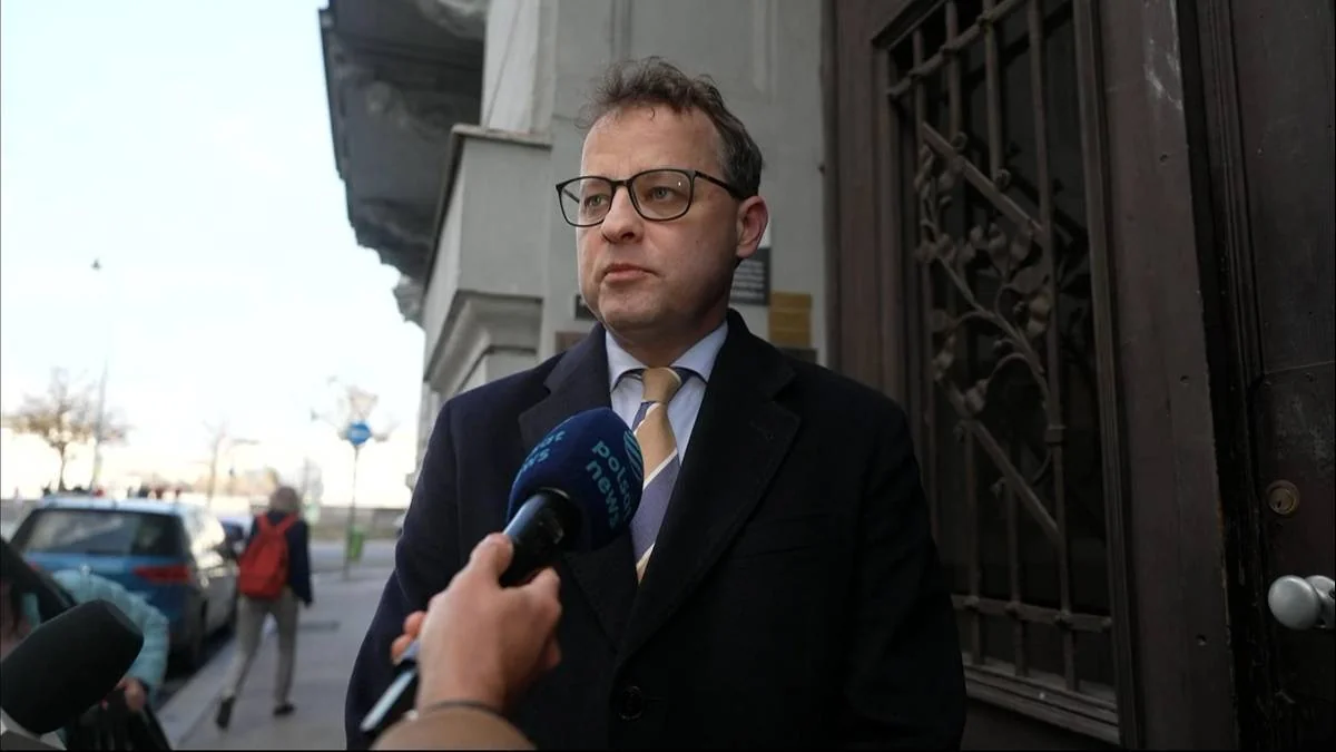 Чоловік в окулярах і темному пальті дає інтерв’ю мікрофону Polsat News біля дверей