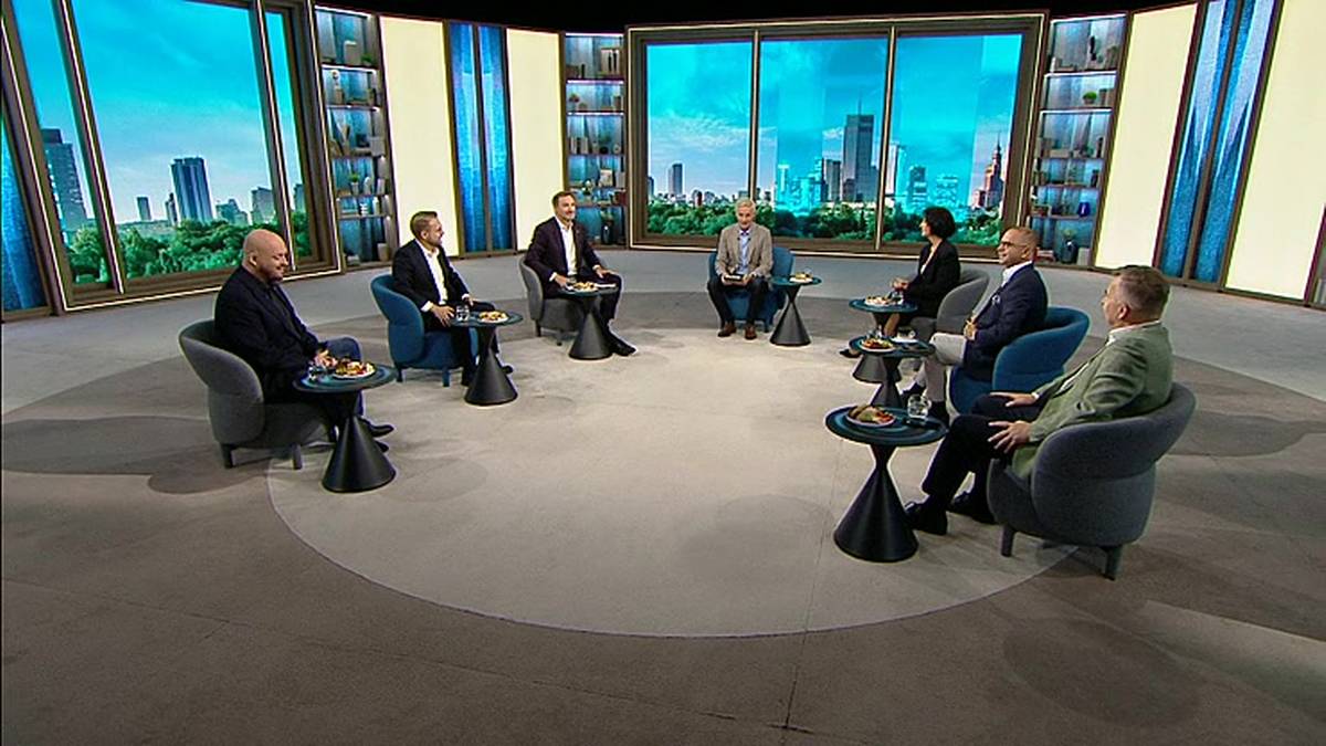 Семеро людей сидять у кріслах колом у телестудії з панорамою міста