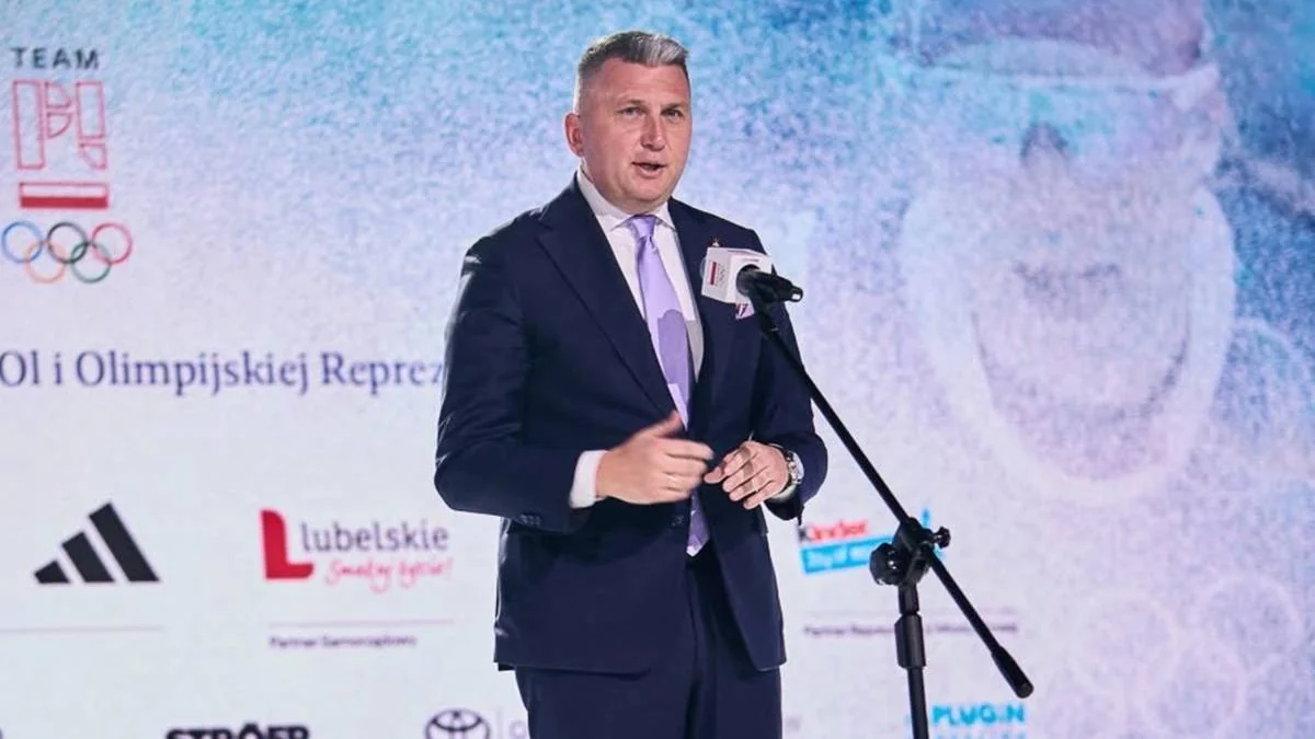 Чоловік у темному костюмі виступає біля мікрофона на тлі логотипів PKOl