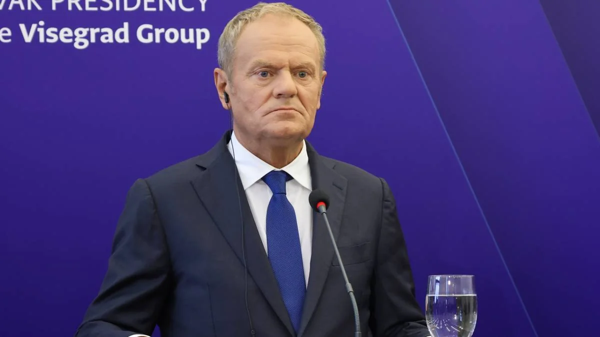 Дональд Туск у костюмі виступає біля мікрофона на тлі Вишеградської групи